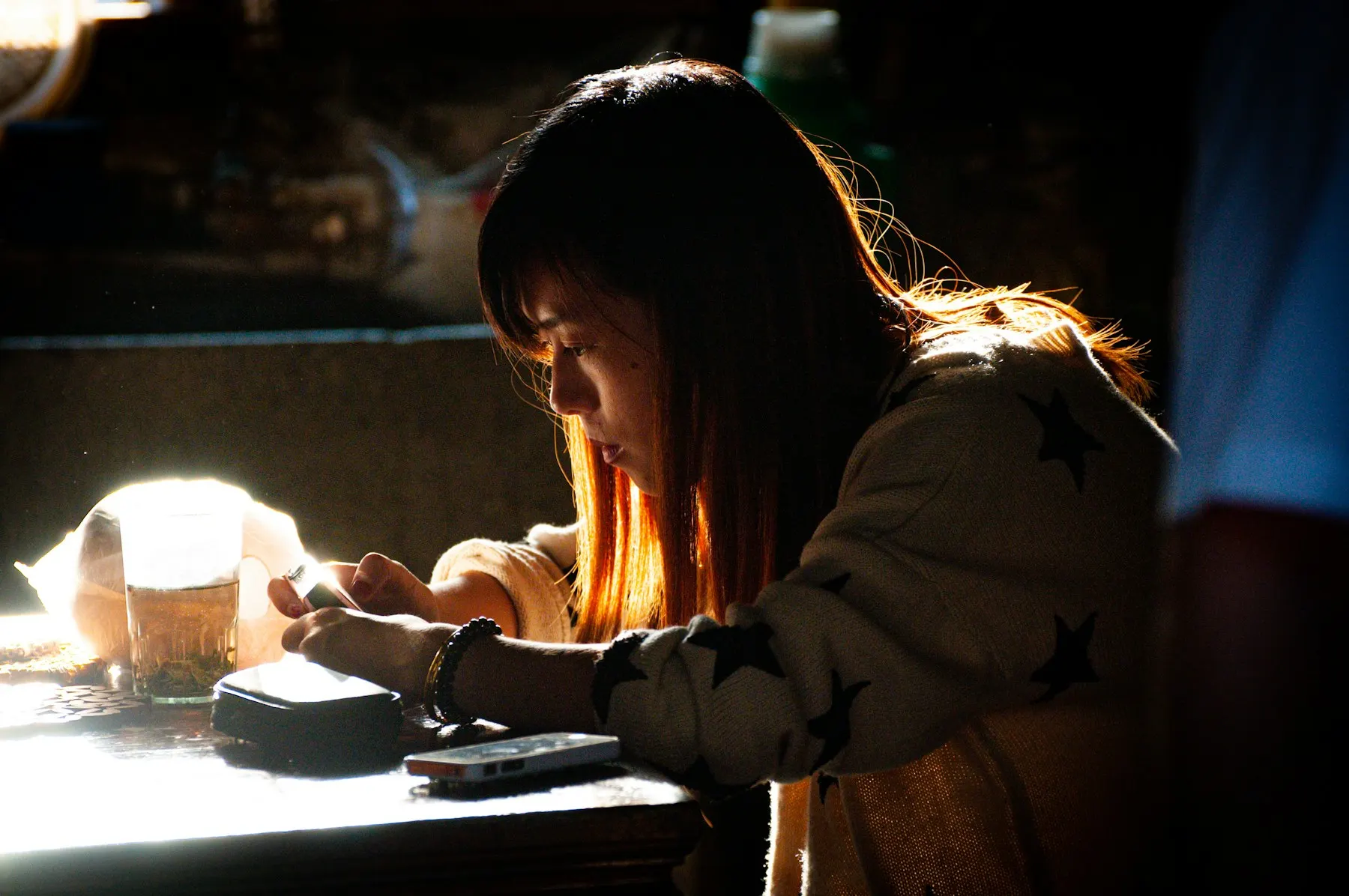 A woman at a desk in warm evening light, reading her phone